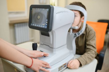 Çocuk göz fraktörüyle göz taramasından geçiyor. Görsel keskinliği kontrol ediyor ve modern klinikte potansiyel görme sorunlarını teşhis ediyor.