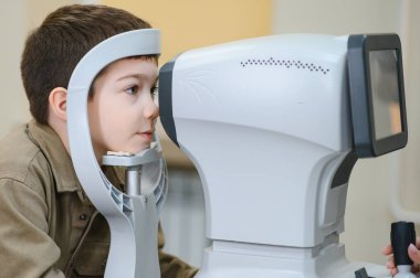 Çocuk görme yeteneğini modern klinikte görme tedavisi için bir teşhis aracı olan otomatik fraktör kullanarak göz doktoru tarafından kontrol ettiriyor.