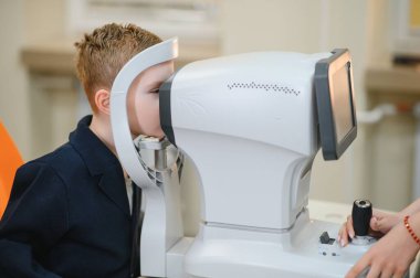 Genç çocuğun vizyonu modern göz hekimliği kliniğinde otomatik fraktör kullanılarak kontrol ediliyor. Çocuklar için yenilikçi göz bakımı teknolojisi.