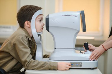 Oftalmolog, bir klinikte otomatik fraktör kullanarak çocuğun görme yeteneğini inceleyerek, doğru görme ve göz bakımını sağlama alıyor.