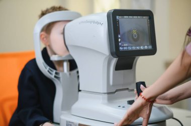Bir göz hekimi kliniğinde bir çocuğun görme yetisini otomatik fraktörle inceleyen doktor, doğru görme ve bakım tanısı koyuyor.