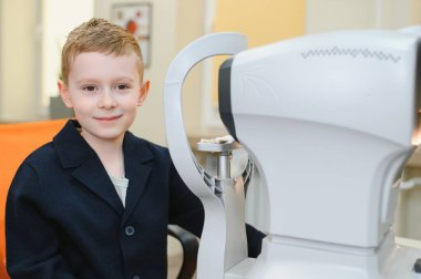 Göz muayenesi sırasında gülümseyen genç bir çocuk göz hekiminde modern bir oto-fraktör kullanıyor.