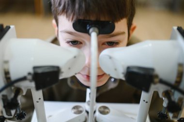 Genç bir çocuğun modern bir göz kliniğinde göz doktoruna görünmesi için phoropter kullanılıyor.