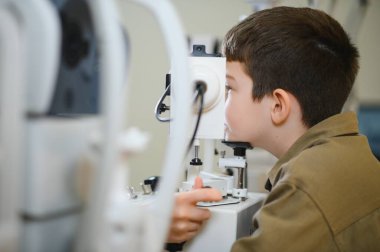 Genç bir çocuk, klinikte modern bir tıbbi cihaz kullanarak bir göz doktoru tarafından kontrol ediliyor.