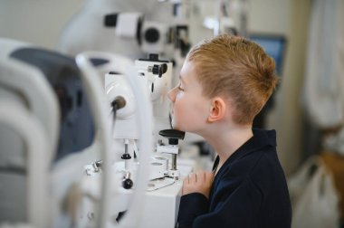 Çocuk, bir göz doktoruyla kontrol için teşhis makinesi kullanıyor. Bir tıp merkezinde görme yetisini kontrol ediyor.
