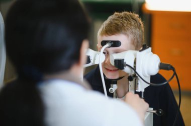 Modern bir klinikte bir göz doktorunun yardımıyla ileri seviye ekipman kullanarak vizyon kontrolü yaptıran bir çocuk.