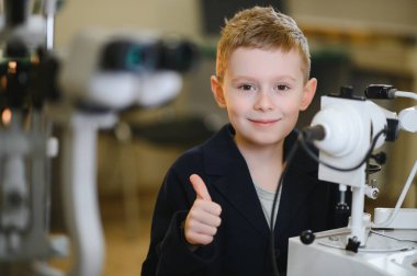 Modern bir klinikte yapılan göz muayenesi sırasında gülümseyen çocuk görme ve tedavi konusunda olumlu bir deneyim gösteriyor.