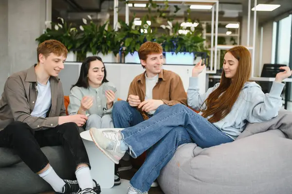 Yeni başlayan dört genç çalışan, modern bir çalışma alanında kart oynayarak tatillerini geçiriyorlar.