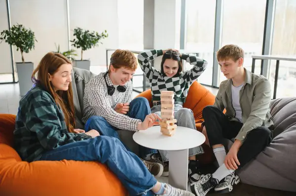Bir grup genç öğrenci boş zamanların tadını çıkarıyor, modern bir çalışma alanında blok istifleme oyunu oynuyorlar.