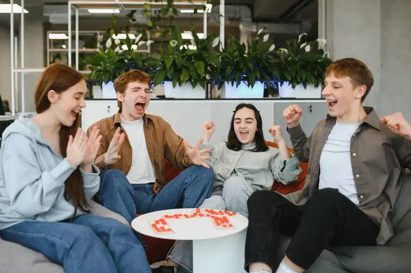 Oyun oynayan dört neşeli arkadaş, zaferlerini modern ofis alanında kutlarken heyecan ve mutluluk ifade ediyorlar.