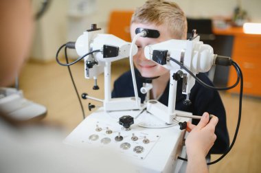 Modern bir klinikte bir göz doktorunun yardımıyla ileri seviye tanı cihazları kullanılarak vizyon kontrolünden geçen genç bir çocuk.