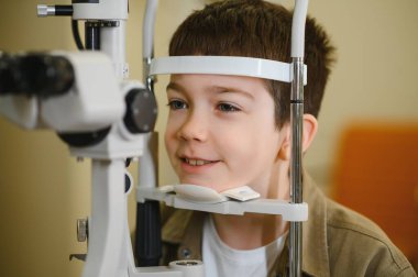Görme testinden geçerken gülümseyen bir çocuk bir göz hekimi kliniğinde, görme yeteneğini kontrol ediyor.