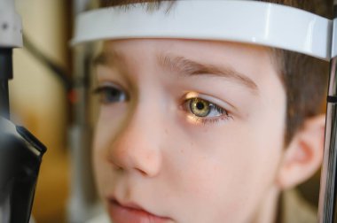 Çocuk hasta, modern bir klinikte phoropter kullanan bir göz doktoru tarafından kontrol ediliyor.