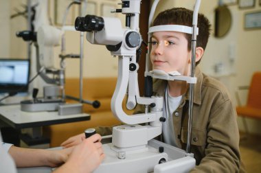 Modern oftalmoloji kliniğinde kesik lamba biyomikroskobu kullanan genç bir çocuğun görme yeteneğini inceleyen oftalmolog.