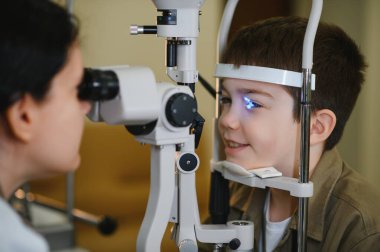 Modern bir klinikte göz ve göz sağlığını güvence altına almak için kesik lamba kullanan göz doktoru tarafından göz muayenesinden geçen genç bir çocuk.
