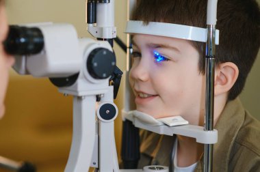 Modern bir klinikte biyomikroskopla göz muayenesi geçiren gülümseyen bir çocuk.