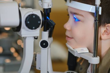 Uzman bir tıbbi cihaz ile görme kontrolünden geçen çocuk, profesyonel bir klinikte olası göz sorunları için tedavi görüyor.