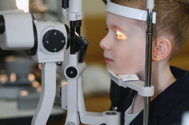 Bir göz sağlığı kliniğinde kesik lamba biyomikroskobu kullanarak görme kontrolünden geçen genç bir çocuk, erken dönem göz bakımının önemini vurguluyor.