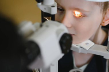 Göz muayenesinden geçen çocuk, bir göz hekimliği kliniğinde özel ekipman kullanılarak, çocukların görme bakımını ve teşhislerini vurguluyor