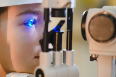Genç bir çocuk, modern bir klinikte mavi ışık tedavisi gören, uzman bir göz hekimi ile görüş kontrolünden geçiyor.