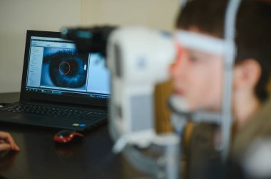 Çocuk göz muayenesinden geçiyor modern bir tanı cihazı kullanarak göz taraması yapıyor ve bilgisayarında göz taraması yapılıyor.