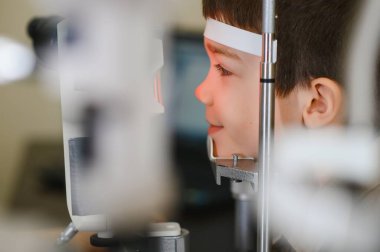 Çocuk hasta, modern bir klinikte phoropter kullanan bir göz doktoru tarafından kontrol ediliyor.