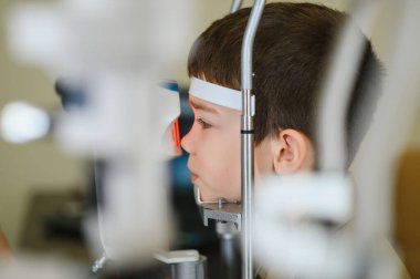 Bir sağlık kliniğinde phoropter kullanan bir göz doktoru tarafından göz muayenesine tabi tutulan bir çocuk, düzgün bir görüş ve teşhis koyuyor.