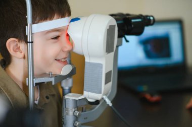 Klinikte modern oftalmolojik ekipman kullanan gülümseyen çocuk görüş kontrolünden geçiyor.