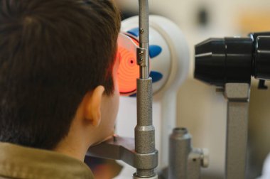 Bir göz hekimi kliniğinde uzman ekipmanlarla görme kontrolünden geçen çocuk, görme sağlığı için kapsamlı bir muayene oluyor.