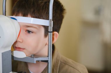 Bir klinikte teşhis cihazı kullanan bir göz doktoru çocuğun görüşünü kontrol ettiriyor.