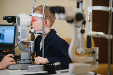 Görme kliniğinde modern bir otorefraktör kullanan bir göz doktoru çocuğun gözlerini kontrol ettiriyor.
