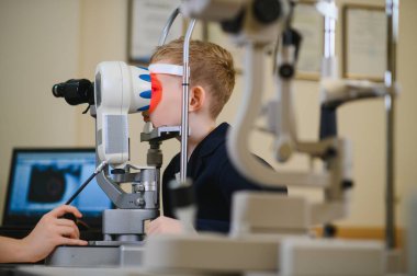 Bir oğlanın görme yeteneğini modern bir göz hekiminde gelişmiş ekipmanlarla inceleyen oftalmolog, optimum görüş bakımı sağlıyordu.