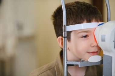 Genç bir çocuğun görüş kliniğinde modern bir tıbbi cihaz kullanarak bir göz doktoru tarafından kontrol edilmesi.