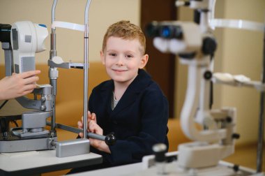 Gülümseyen çocuk göz muayenesinden geçiyor. Optalmoloji kliniğinde modern tıbbi malzemeler kullanılıyor.