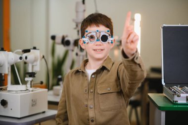 Göz doktorunun muayenesinde parmağıyla işaret eden mahkeme çerçevesi takan genç bir çocuk.