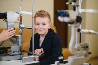 Gülümseyen çocuk, pediatrik göz hastalıkları kliniğinde ileri tıbbi ekipmanlarla görme kontrolü alıyor.