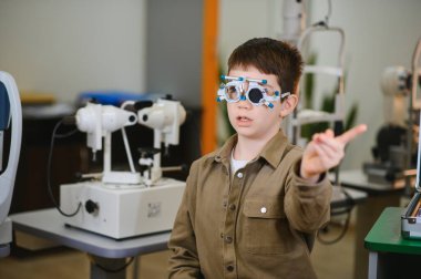 Göz muayenesinden geçen, bir göz kliniğinde deneme aşamasında parmağıyla işaret eden küçük çocuk.