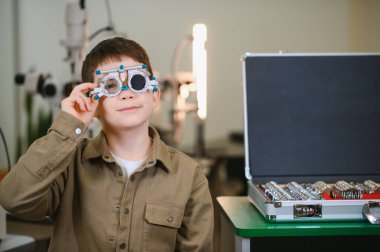 Bir sağlık kliniğinde yapılan göz muayenesi sırasında bir deneme çerçevesi takan çocuk, bir sağlık uzmanının görüş ve göz sağlığını değerlendirir.