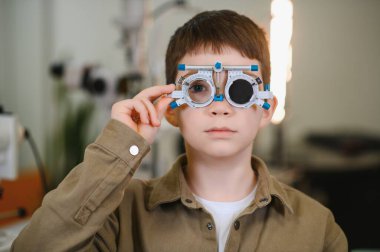 Bir göz doktorunun muayenehanesinde göz muayenesinden geçerken, görüş tanılarına odaklanan bir çocuk.