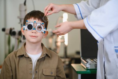 Göz doktoruyla vizyon testine giren çocuk klinikte deneme aşamasında, görsel keskinlik ve göz sağlığını kontrol ediyor.