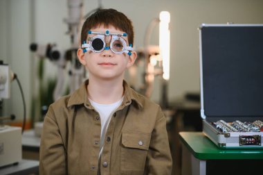 Bir vizyon kliniğinde göz muayenesi sırasında deneme çerçevesi takan genç bir çocuk.