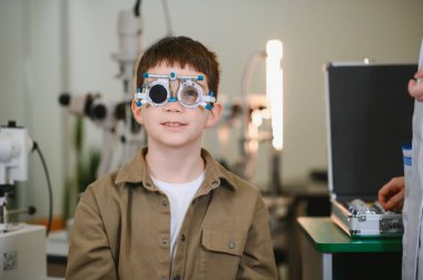 Göz muayenesi sırasında deneme çerçevesi takan çocuk, göz doktorunun ofisinde profesyonel bakım alıyor, düzgün görme değerlendirmesi sağlıyordu.