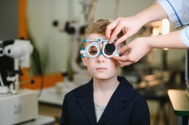 Bir tıp kliniğinde görme düzeltmesi için deneme çerçevesi kullanan genç bir çocuğun görme duyusunu inceleyen oftalmolog.