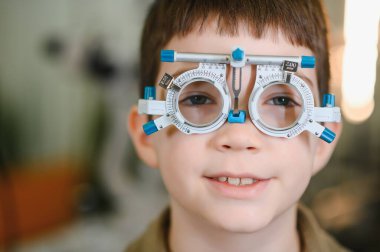 Deneme çerçevesi takan gülümseyen çocuk göz doktorunun ofisinde göz muayenesinden geçiyor.