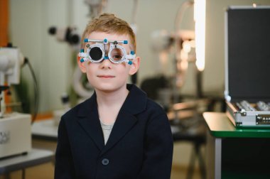 Bir göz doktorunun muayenehanesinde göz muayenesi yapılırken, görme sağlığı ve bakımı üzerine çalışan bir çocuk.