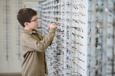 Bir optik mağazada gözlük takan bir çocuk dünyayı daha net görmeye ve görme yeteneğini geliştirmeye hevesle hazırlanıyor.