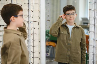 Gözlüklerini bir gözlükçüde aynanın önünde ayarlayan bir çocuk, daha iyi bir görüş için daha şık bir çerçeve seçiyor.