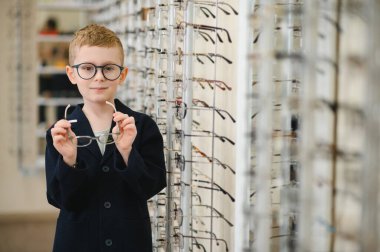Bir optik mağazada yeni gözlük deneyen çocuk, gelişmiş görme ve neşeli bir gülümsemeyle gelişmiş göz sağlığına hazırlanıyor.
