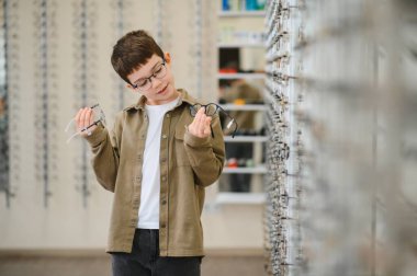 Çocuk bir optik mağazada iki gözlük karşılaştırıyor, vizyon düzeltmesi hakkında karar veriyor.