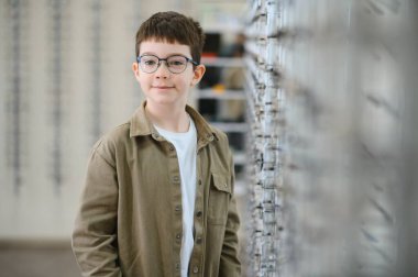 Gülümseyen ve yeni gözlük takan bir çocuk bir optik mağazada çerçeveleri seçerken, gelişmiş görüş ve sağlık hizmetlerinin keyfini çıkarıyor